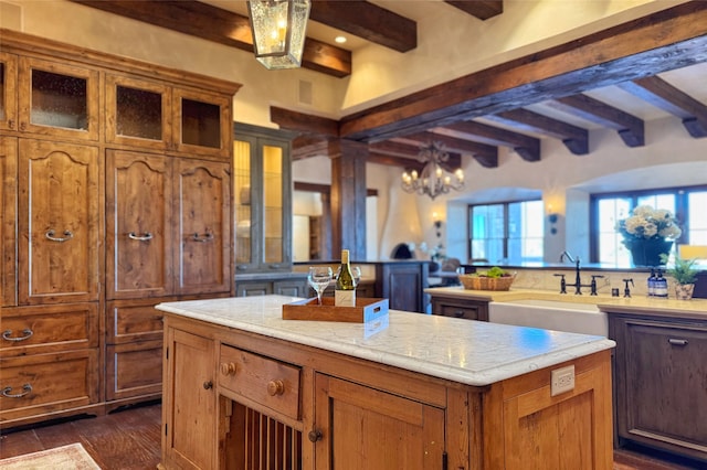 kitchen with beam ceiling, a sink, dark wood-type flooring, brown cabinets, and a center island