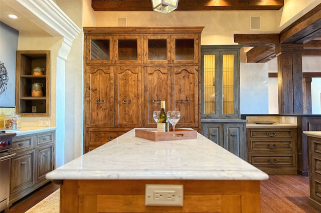 kitchen featuring built in features, light stone counters, brown cabinetry, dark wood-type flooring, and a center island