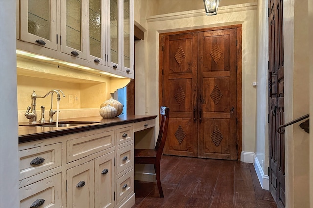 kitchen featuring dark countertops, a sink, glass insert cabinets, white cabinets, and dark wood-style flooring