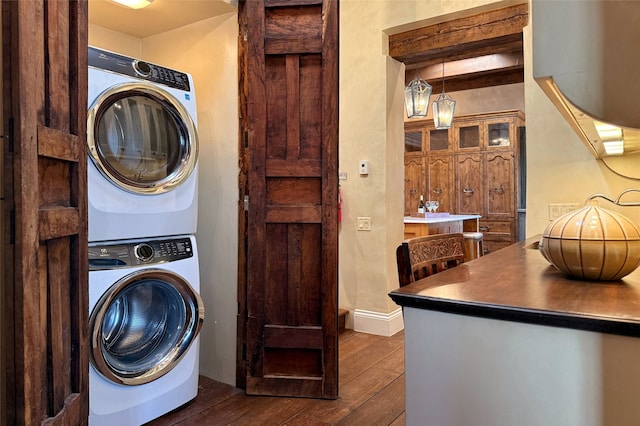 washroom featuring laundry area, baseboards, stacked washer and clothes dryer, and dark wood-type flooring