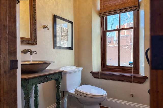 half bathroom with a sink, baseboards, and toilet