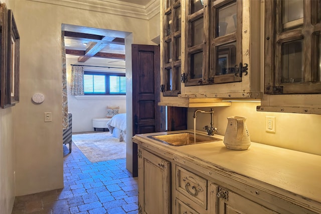 kitchen with glass insert cabinets, beamed ceiling, light countertops, brick floor, and a sink