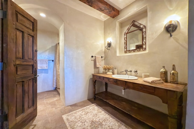 full bath featuring a sink, beamed ceiling, a shower with shower curtain, and stone finish floor