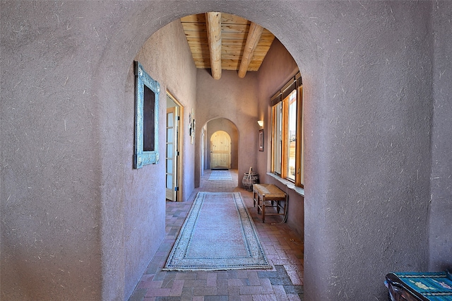 corridor featuring beam ceiling, brick floor, arched walkways, wood ceiling, and a textured wall