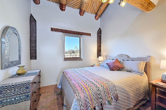 bedroom with beamed ceiling, a high ceiling, and brick floor