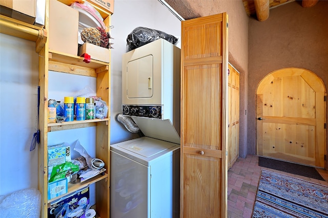 clothes washing area with laundry area, brick floor, and stacked washer and clothes dryer