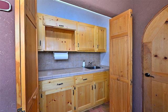 kitchen featuring tile countertops, tasteful backsplash, light brown cabinets, and a sink