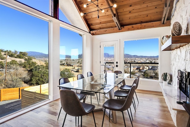 dining area featuring a stone fireplace, a mountain view, lofted ceiling with beams, and wood-type flooring