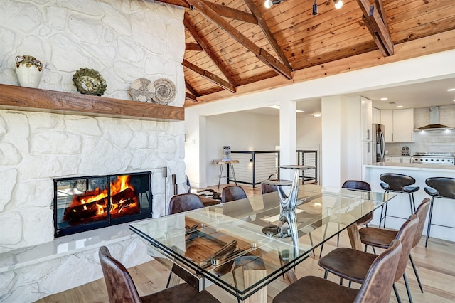 dining room featuring wood ceiling, light wood-type flooring, a stone fireplace, and lofted ceiling with beams