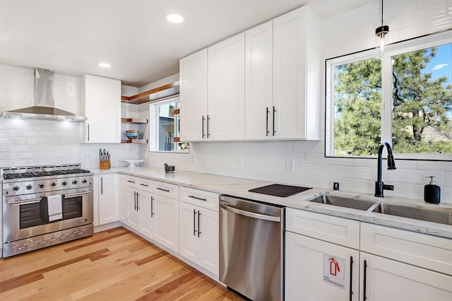 kitchen with light wood finished floors, open shelves, a sink, stainless steel appliances, and wall chimney range hood