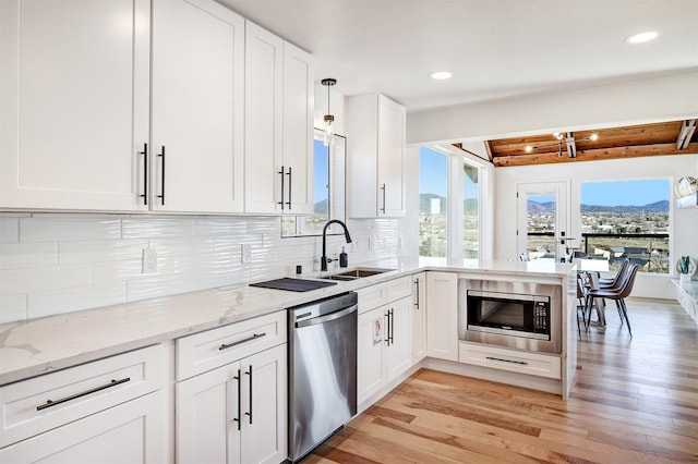 kitchen featuring light wood-style flooring, a sink, appliances with stainless steel finishes, white cabinetry, and backsplash