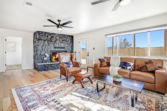 living room featuring a ceiling fan, wood finished floors, a fireplace, and visible vents