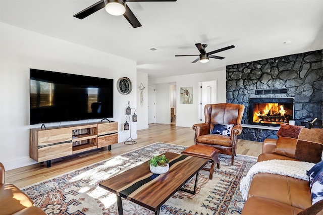 living room with wood finished floors, baseboards, visible vents, a fireplace, and ceiling fan