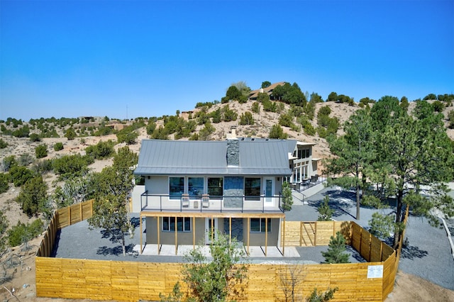 rear view of house featuring stucco siding, metal roof, a fenced backyard, a balcony, and a standing seam roof