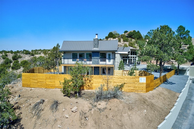 back of property with fence, a chimney, metal roof, a balcony, and a standing seam roof