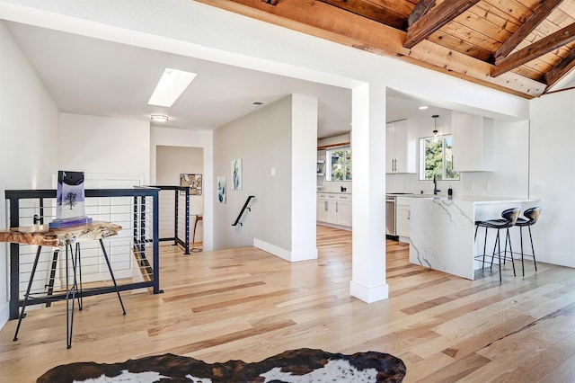 interior space featuring visible vents, lofted ceiling with skylight, light wood finished floors, baseboards, and wood ceiling