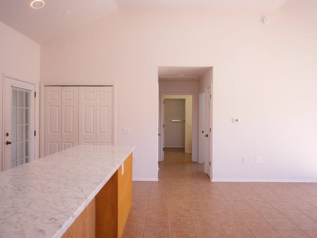 kitchen featuring light tile patterned floors, light stone counters, high vaulted ceiling, and baseboards