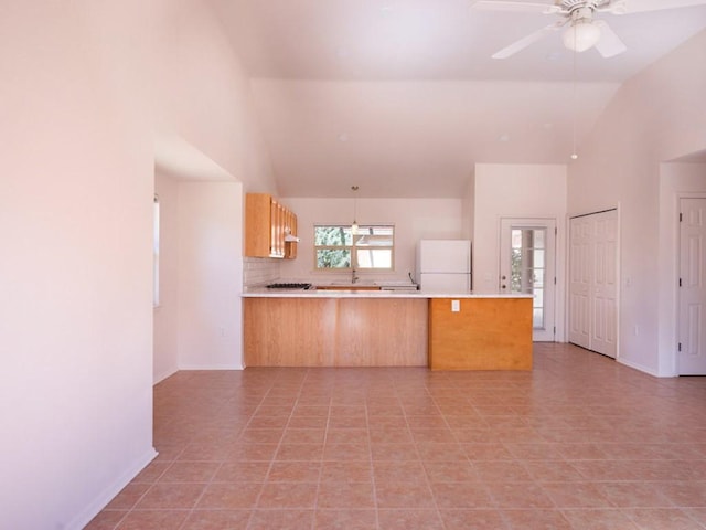 kitchen featuring backsplash, ceiling fan, light countertops, a peninsula, and freestanding refrigerator