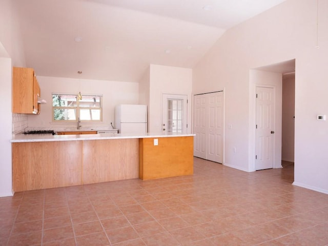 kitchen with under cabinet range hood, freestanding refrigerator, a peninsula, light countertops, and decorative backsplash