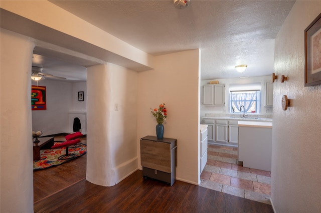 hallway with a sink, wood finished floors, baseboards, and a textured ceiling