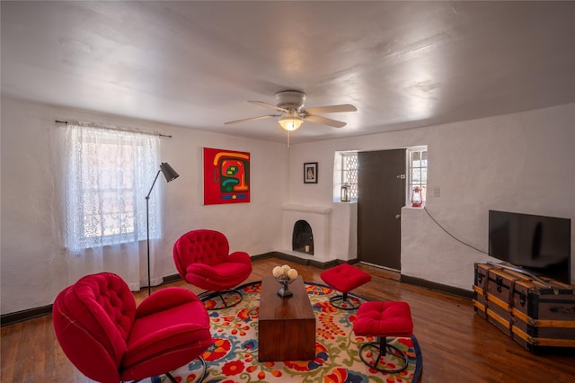 living room featuring a ceiling fan, wood finished floors, baseboards, and a fireplace with raised hearth