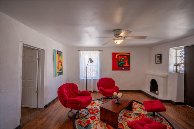 living area with ceiling fan, baseboards, wood finished floors, and a fireplace with raised hearth