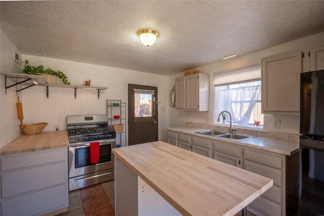 kitchen featuring stainless steel gas range oven, butcher block countertops, a sink, a center island, and freestanding refrigerator