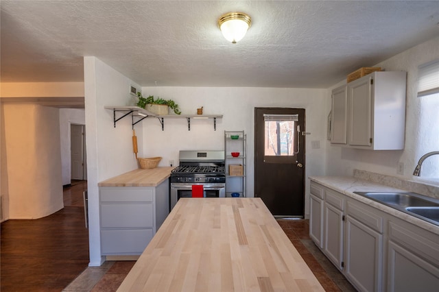 kitchen featuring stainless steel gas range oven, a sink, a textured ceiling, wood counters, and open shelves