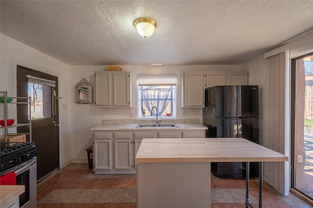 kitchen featuring a sink, wood counters, freestanding refrigerator, gas range, and a healthy amount of sunlight