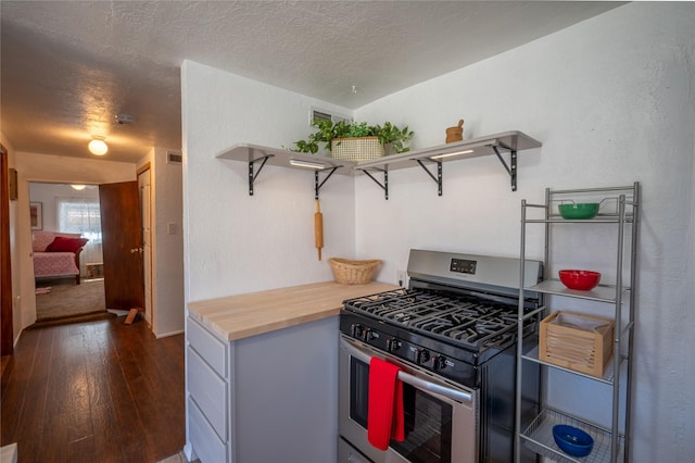 kitchen featuring open shelves, dark wood-style floors, stainless steel range with gas stovetop, and a textured ceiling