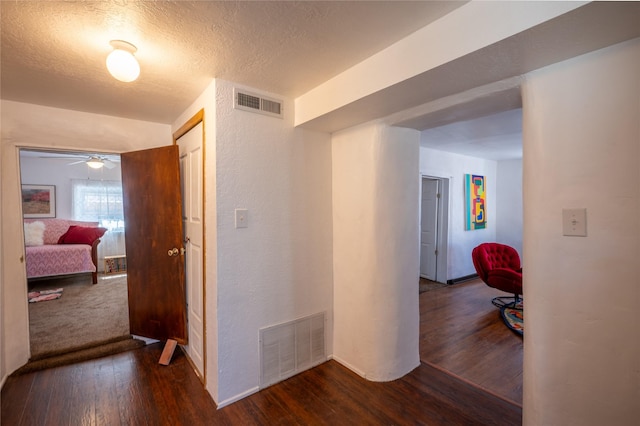 corridor featuring visible vents, a textured ceiling, wood finished floors, and a textured wall