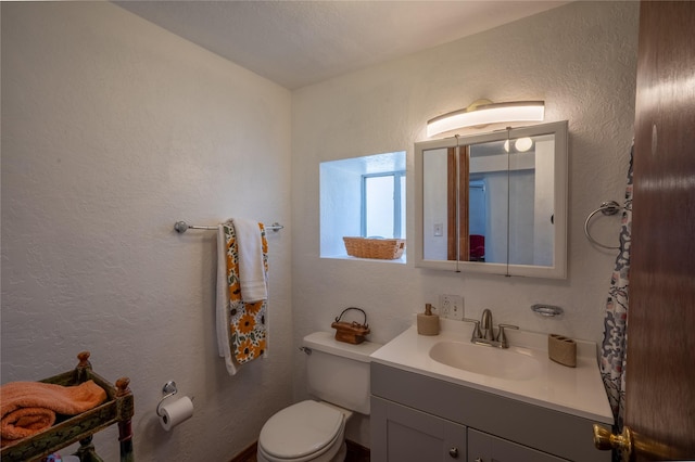 half bathroom featuring toilet, vanity, and a textured wall