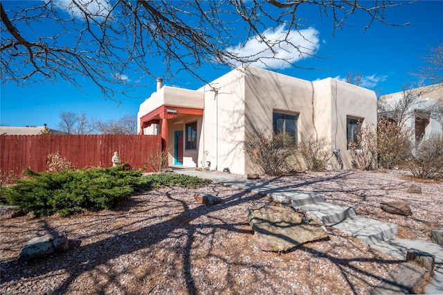 view of home's exterior featuring stucco siding, a chimney, and fence