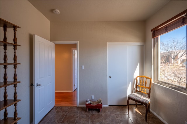 living area featuring dark tile patterned flooring, a textured wall, and baseboards