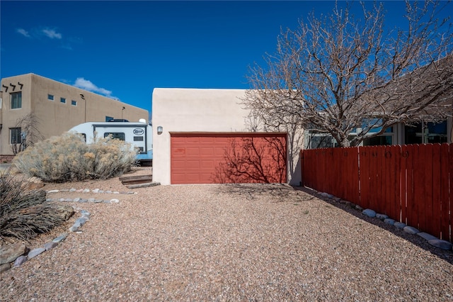 exterior space featuring stucco siding, gravel driveway, a garage, and fence