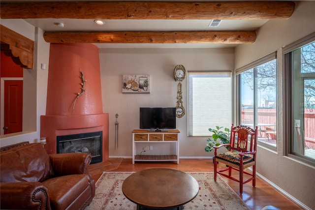 living area featuring wood finished floors, visible vents, baseboards, beamed ceiling, and a large fireplace