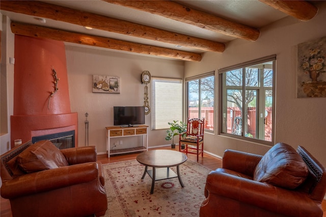 living room featuring beamed ceiling, a large fireplace, baseboards, and wood finished floors