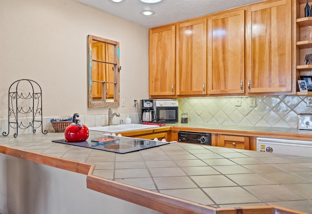 kitchen with tile countertops, open shelves, a sink, black dishwasher, and backsplash