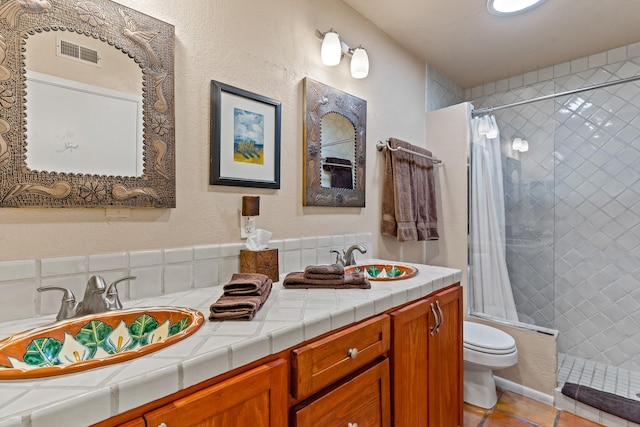 full bath with toilet, visible vents, a tile shower, and a sink