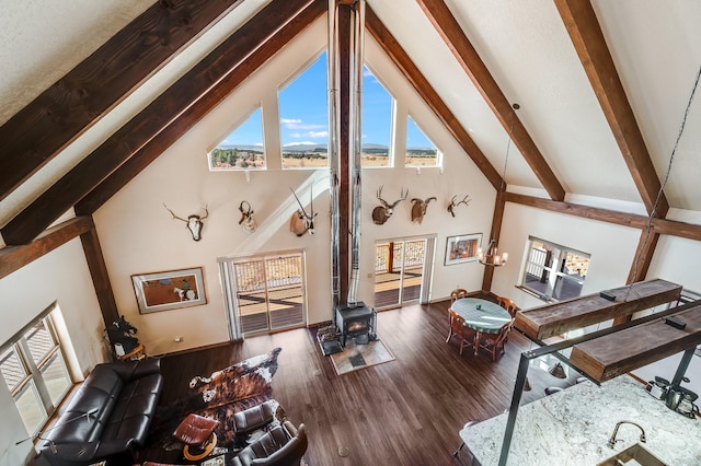 living area featuring beam ceiling, a wood stove, wood finished floors, and high vaulted ceiling