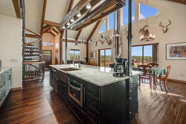 kitchen with dark cabinetry, dark wood-style floors, high vaulted ceiling, an island with sink, and a chandelier