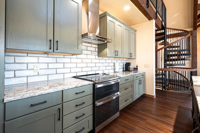 kitchen with double oven range, gray cabinets, dark wood-type flooring, wall chimney exhaust hood, and backsplash