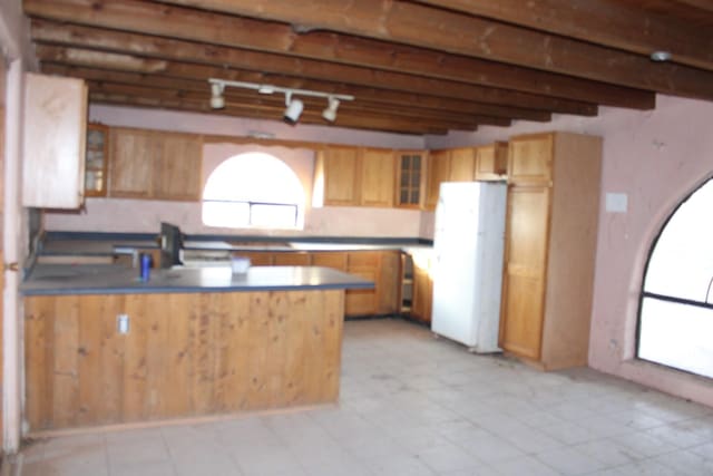 kitchen with a peninsula, beam ceiling, freestanding refrigerator, rail lighting, and glass insert cabinets