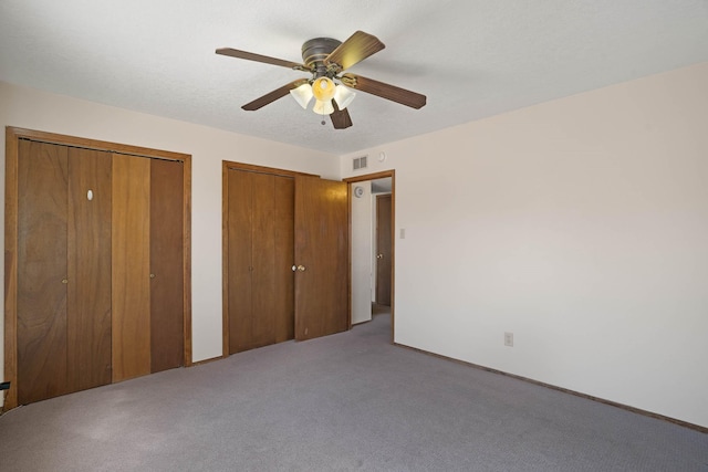 unfurnished bedroom with a textured ceiling, two closets, a ceiling fan, and carpet floors