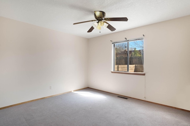 carpeted empty room with visible vents, a textured ceiling, baseboards, and ceiling fan