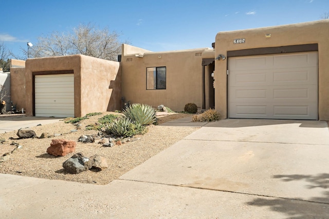 pueblo-style house featuring an attached garage, driveway, and stucco siding