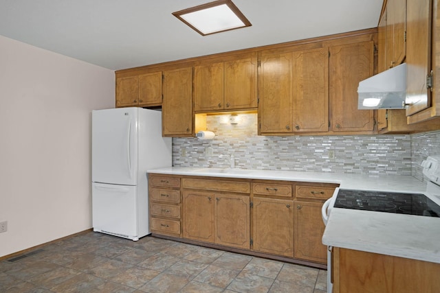 kitchen with white appliances, brown cabinetry, under cabinet range hood, and a sink