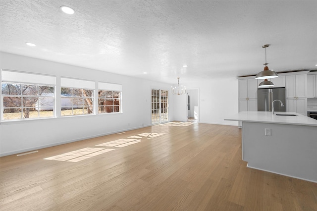 unfurnished living room featuring visible vents, a sink, light wood-style floors, a textured ceiling, and a notable chandelier