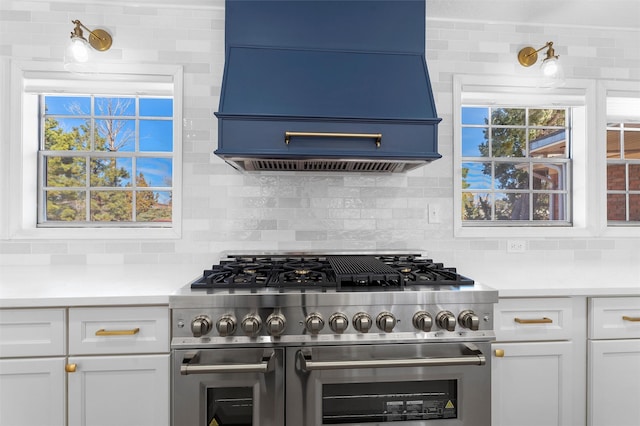 kitchen featuring double oven range, backsplash, white cabinets, light countertops, and custom exhaust hood