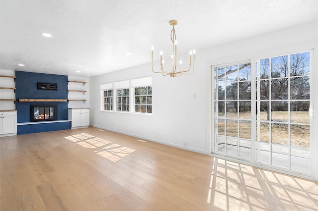 unfurnished living room featuring a large fireplace, baseboards, a chandelier, light wood-style flooring, and a textured ceiling